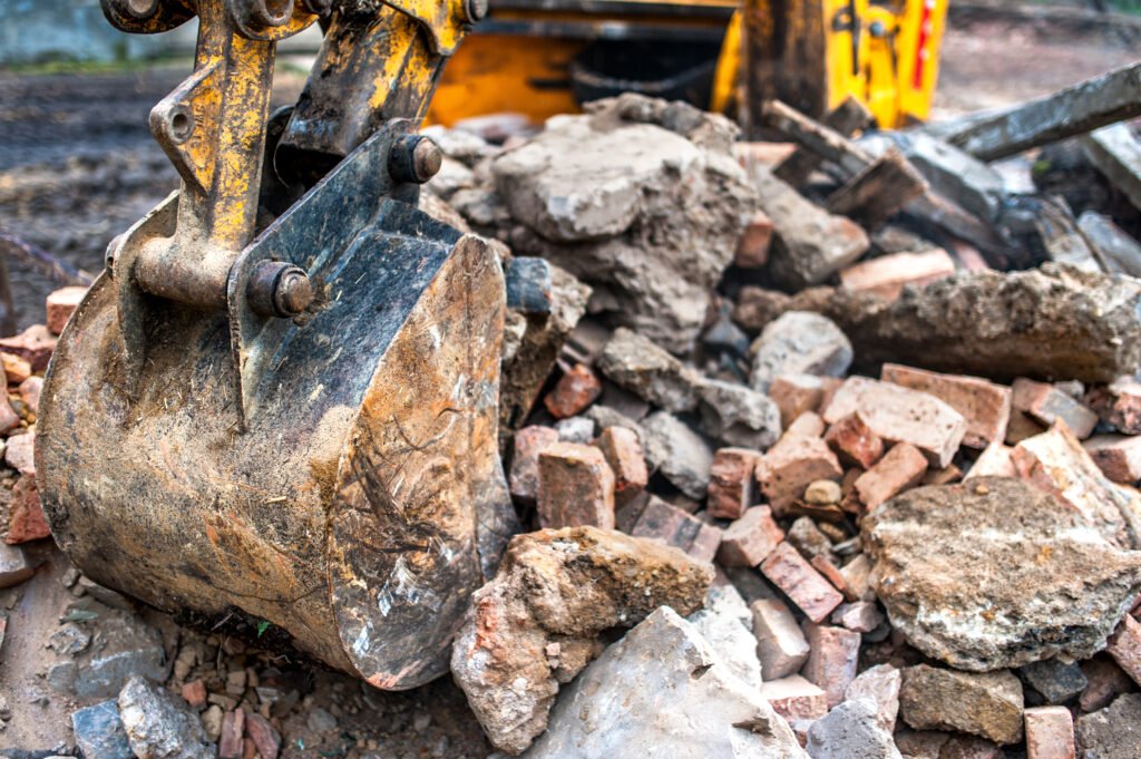 close-up of excavator bucket loading rocks, stones, earth and concrete bricks from demolition site