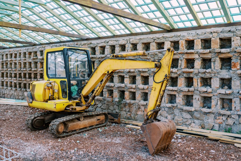 Yellow excavator working in a large brick greenhouse. High quality photo